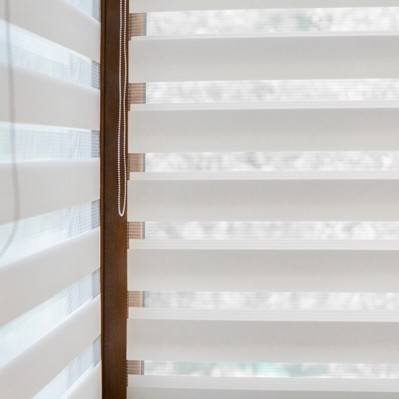 Details of white fabric roller blinds on the plastic window with wood texture in the living room