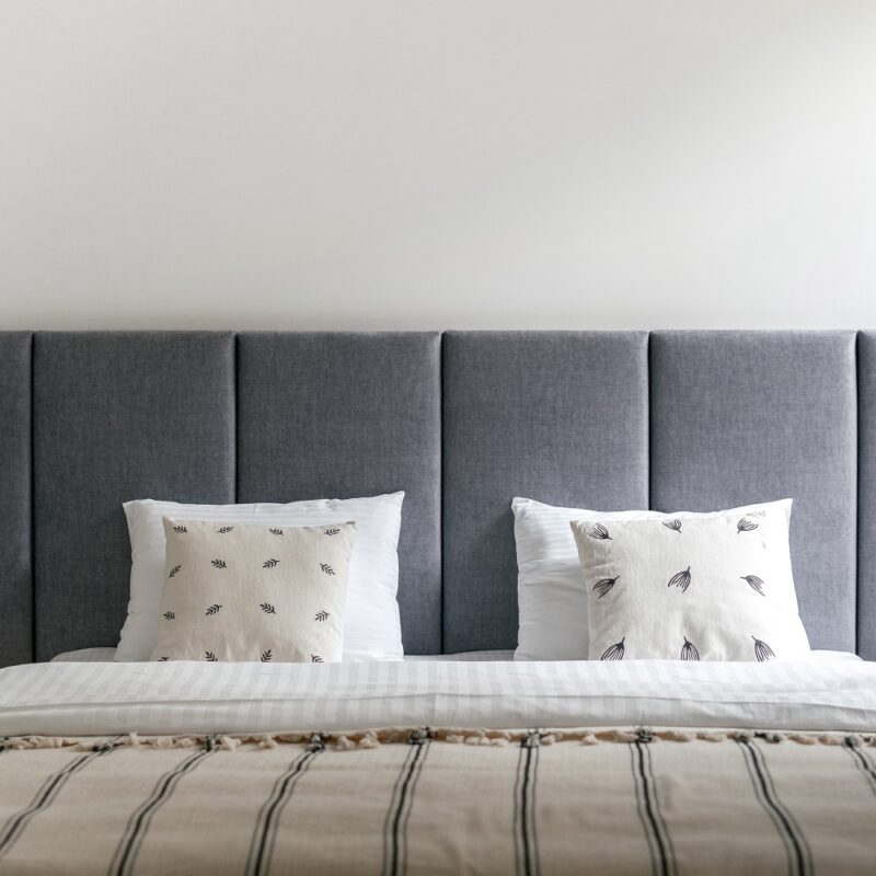 Bedroom interior, bed at modern apartment design. Furniture bedhead with pillows in home. Closeup at cozy scandi room with white bedding decor, blanket. Loft lamp hanging from above.